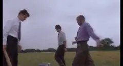 Three men destroy a computer in a field