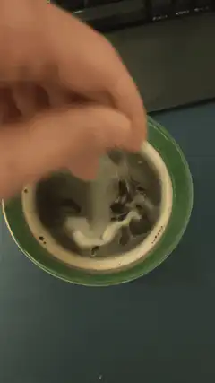 Hand stirring coffee in a green mug