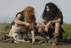 Two cavemen preparing food outdoors