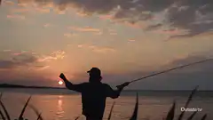 Silhouette of man fly fishing at sunset