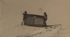 Two people carrying a snow fence