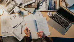 Hands editing a document at a cluttered desk